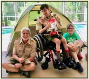 Scout in wheelchair in front of a tent with parents.